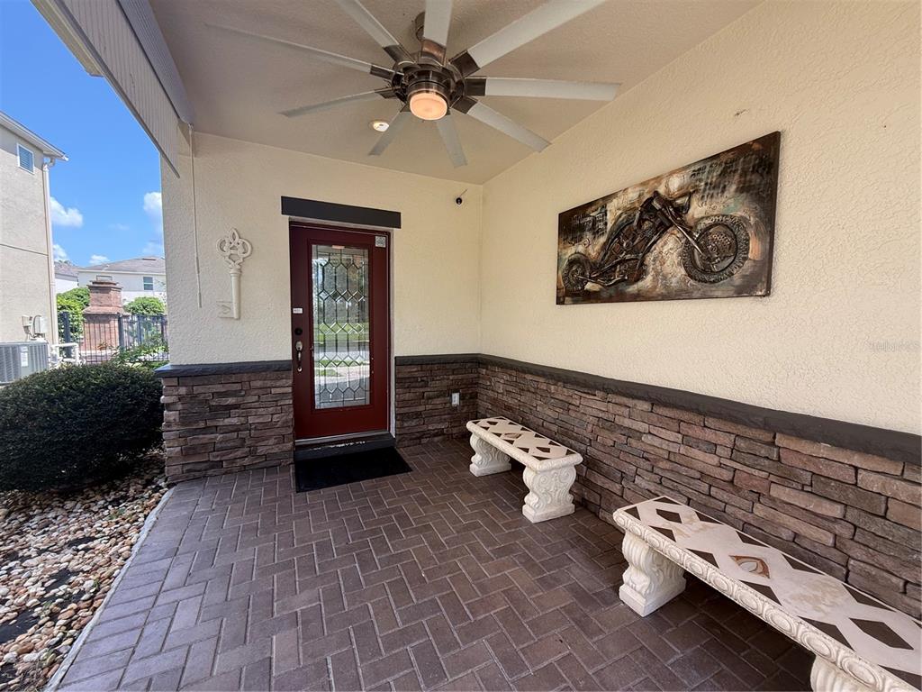 A covered porch features stone siding, two stone benches, a ceiling fan, and a red door — 2706 MONTICELLO WAY, KISSIMMEE, FL