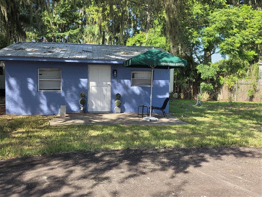 A blue, single-story building with a metal roof and a patio featuring a green umbrella — 10446 COUNTY ROAD 44, LEESBURG, FL
