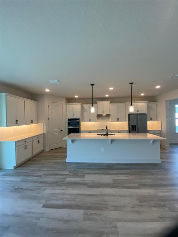 An open-concept living room and kitchen feature white cabinetry, a large island, and wood flooring — 9493 EMERALD BERRY DRIVE, WINTER GARDEN, FL