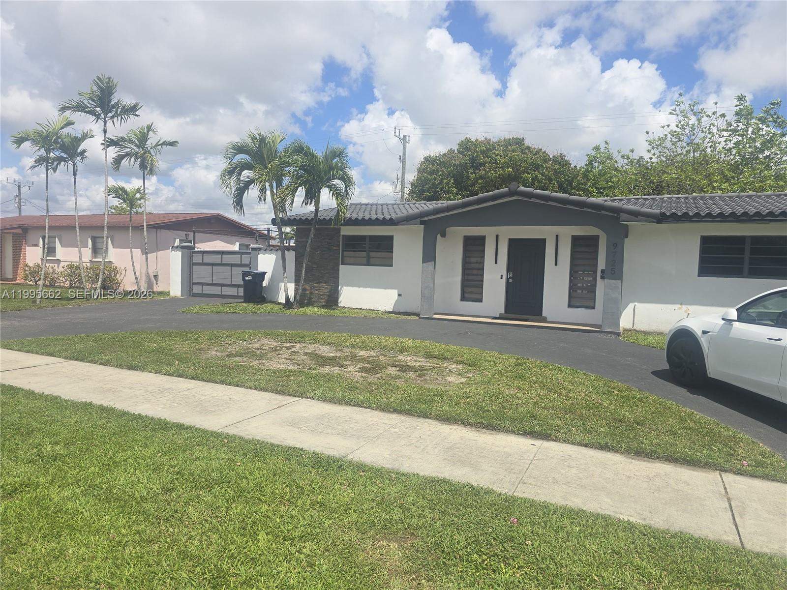 A white single-story house features a dark roof, a paved driveway, and palm trees — 9725 SW 15th St, Miami FL 33174, MIAMI, FL