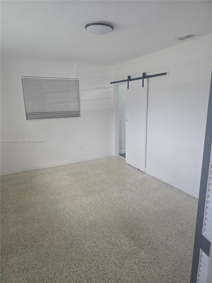 A bedroom features white walls, a sliding barn door, and speckled flooring — 9725 SW 15th St, Miami FL 33174, MIAMI, FL