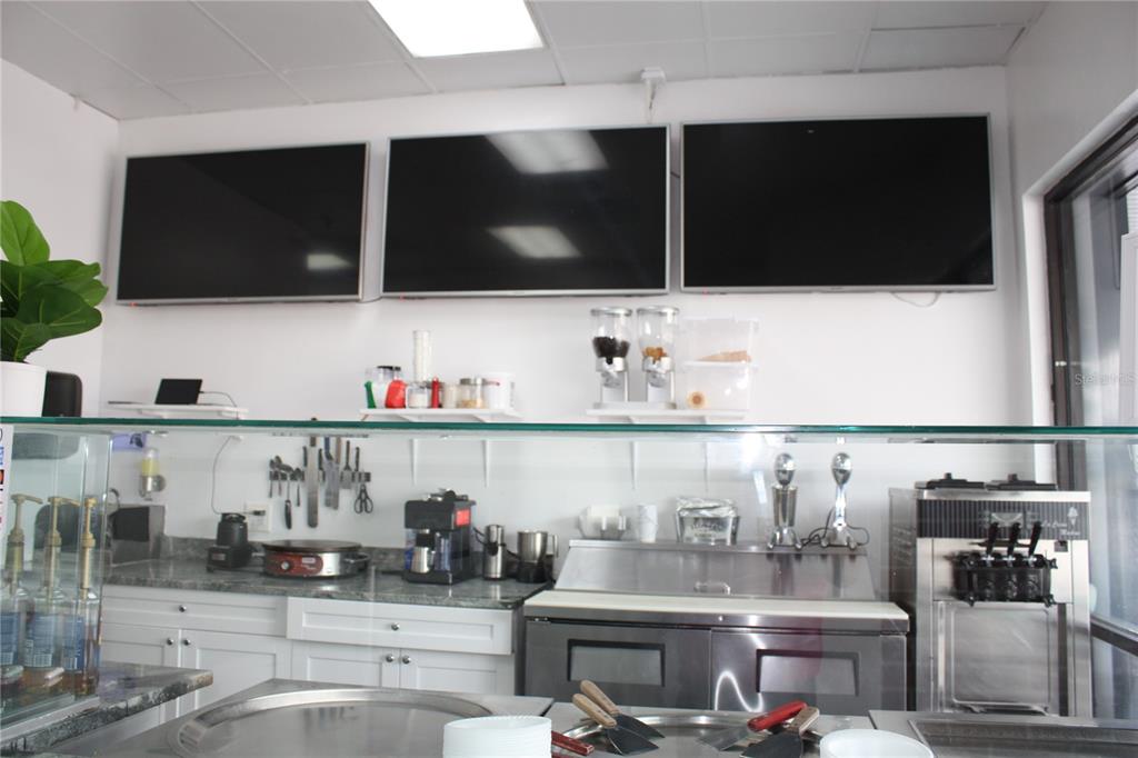 This commercial kitchen features stainless steel equipment, white cabinetry, and three wall-mounted televisions — 2454 MCMULLEN BOOTH ROAD UNIT 303, CLEARWATER, FL