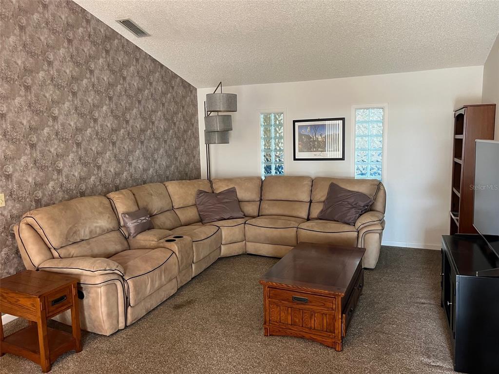 A living room features a large tan sectional sofa, a wooden coffee table, and wallpaper — 330 BONNIE LANE, ORANGE CITY, FL