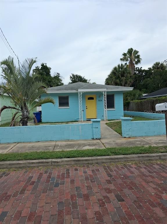 A light blue house with a yellow front door sits behind a matching block wall — 217 BANANA STREET, TARPON SPRINGS, FL