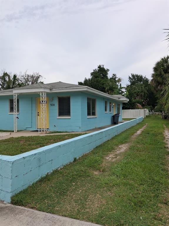 A light blue, single-story concrete block house features a yellow front door and a low wall — 217 BANANA STREET, TARPON SPRINGS, FL