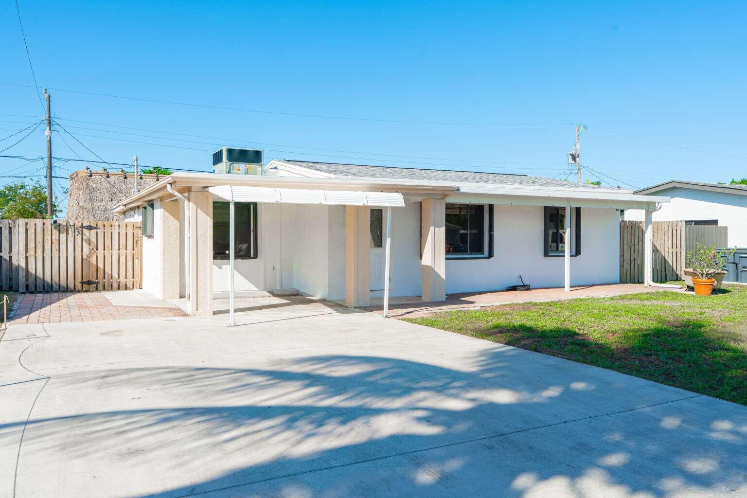 A white single-story house features a concrete driveway, a covered patio, and a wooden fence — 3110 Scanlan Avenue, Lake Worth FL 33461, LAKE WORTH, FL