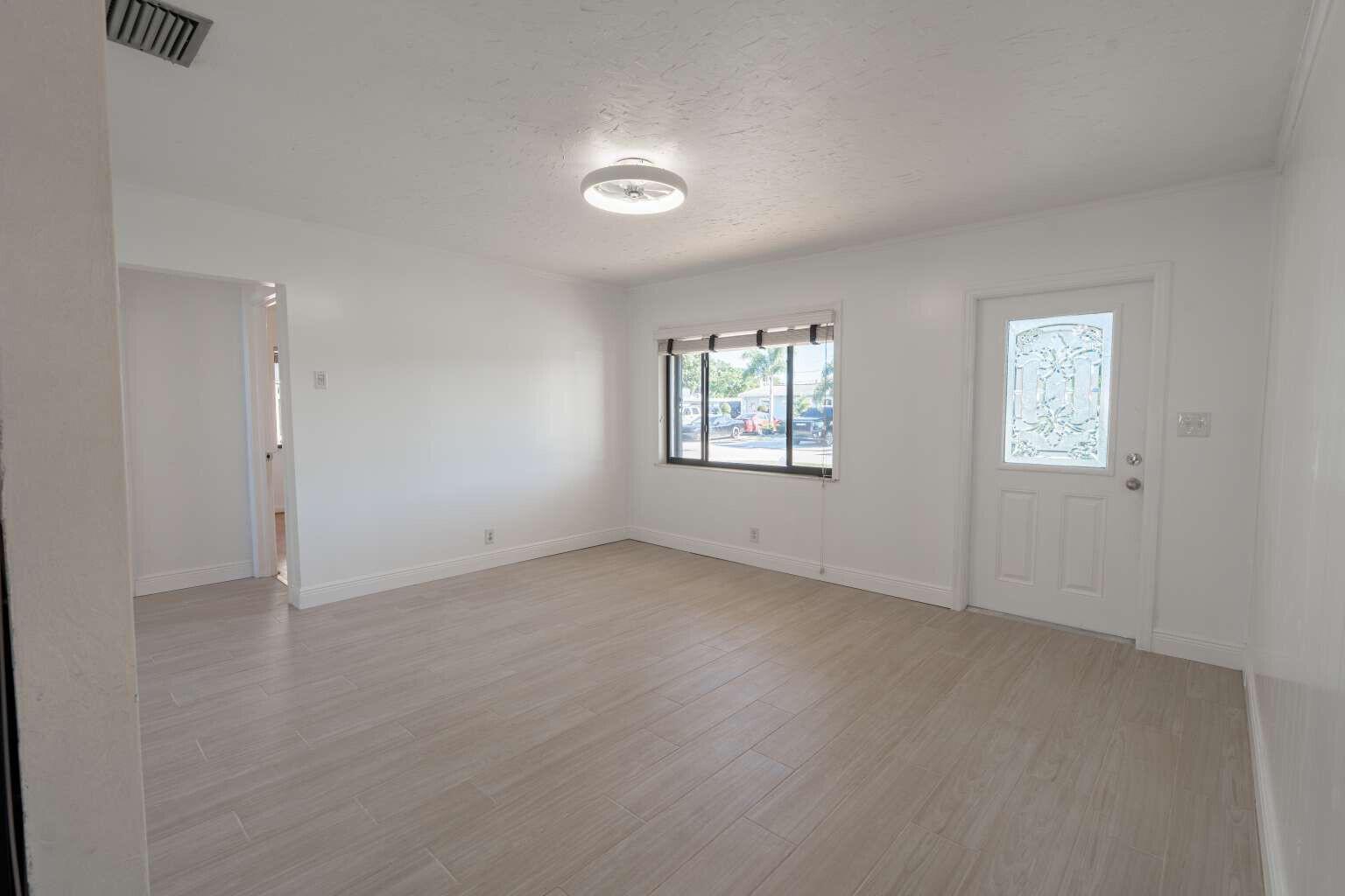 An empty living room with white walls, light wood-look tile flooring, and a front door — 3110 Scanlan Avenue, Lake Worth FL 33461, LAKE WORTH, FL
