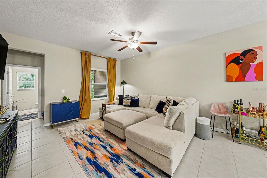 A living room features a beige sectional sofa, a colorful area rug, and yellow curtains — 4524 TUSCAN LOON DRIVE, TAMPA, FL