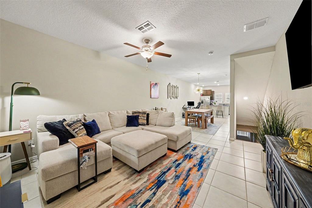 A living room with a beige sectional sofa, tile flooring, and an open dining area — 4524 TUSCAN LOON DRIVE, TAMPA, FL