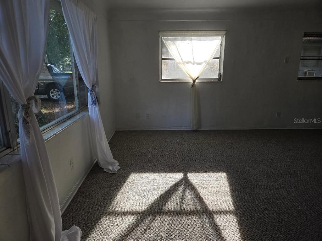 A carpeted room with white walls, two windows with curtains, and sunlight casting shadows — 5715 21ST AVENUE S, GULFPORT, FL