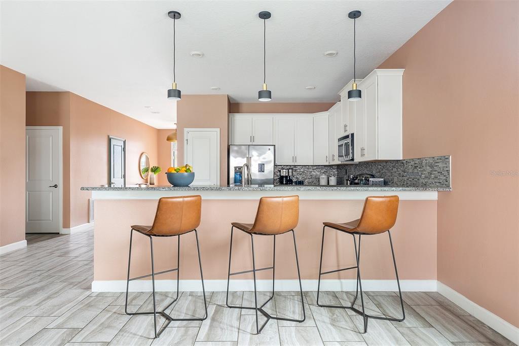 A kitchen features white cabinets, a granite countertop, and three brown bar stools — 1518 ROLLING FAIRWAY DRIVE, DAVENPORT, FL
