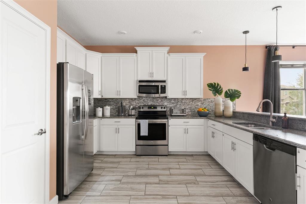 A kitchen features white cabinets, stainless steel appliances, granite countertops, and light wood-look tile flooring — 1518 ROLLING FAIRWAY DRIVE, DAVENPORT, FL