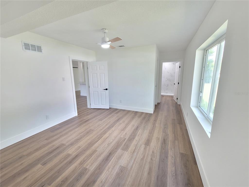 A bedroom with white walls, wood-look flooring, a ceiling fan, and two doorways leading to other rooms — 8 FLAMEVINE LANE, DEBARY, FL