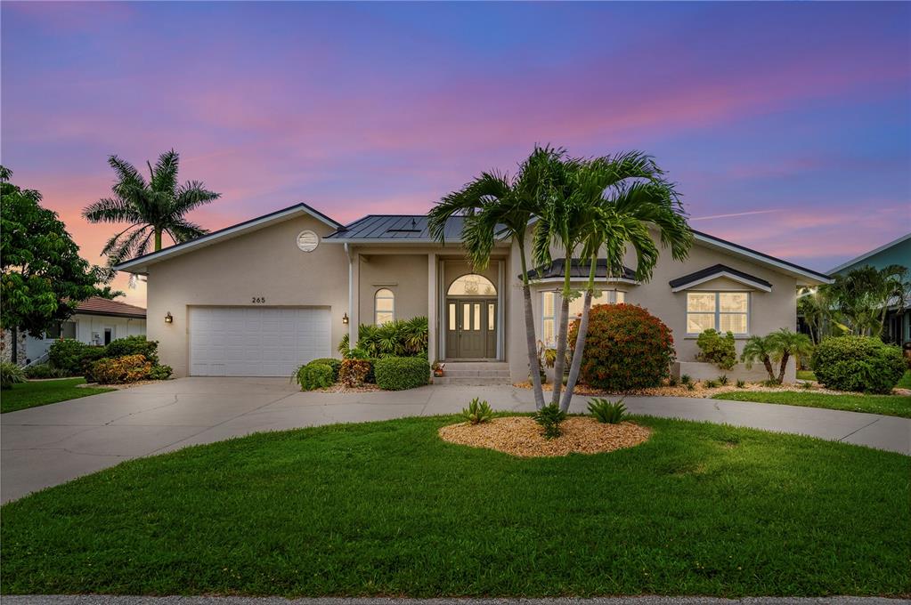 A single-story house with a white garage, arched front door, and palm trees at sunset — 265 BELVEDERE COURT, PUNTA GORDA, FL