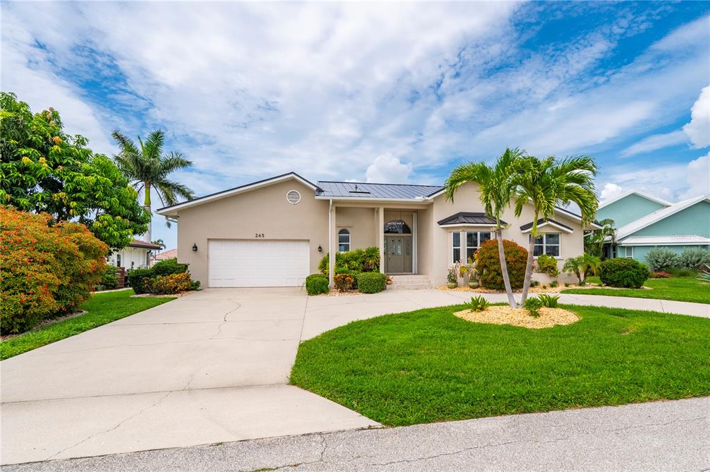 A single-story house with a white garage, beige stucco exterior, and palm trees in front — 265 BELVEDERE COURT, PUNTA GORDA, FL