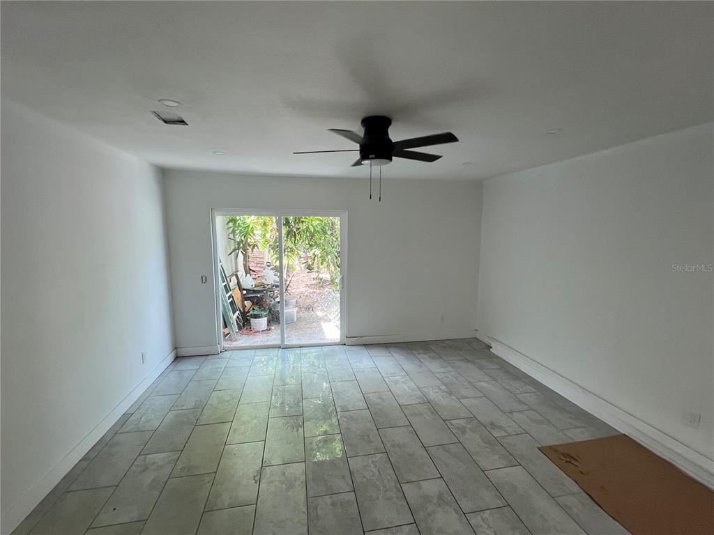 A room with white walls, gray tile flooring, a ceiling fan, and sliding glass doors — 6138 OAK CLUSTER CIRCLE, TAMPA, FL