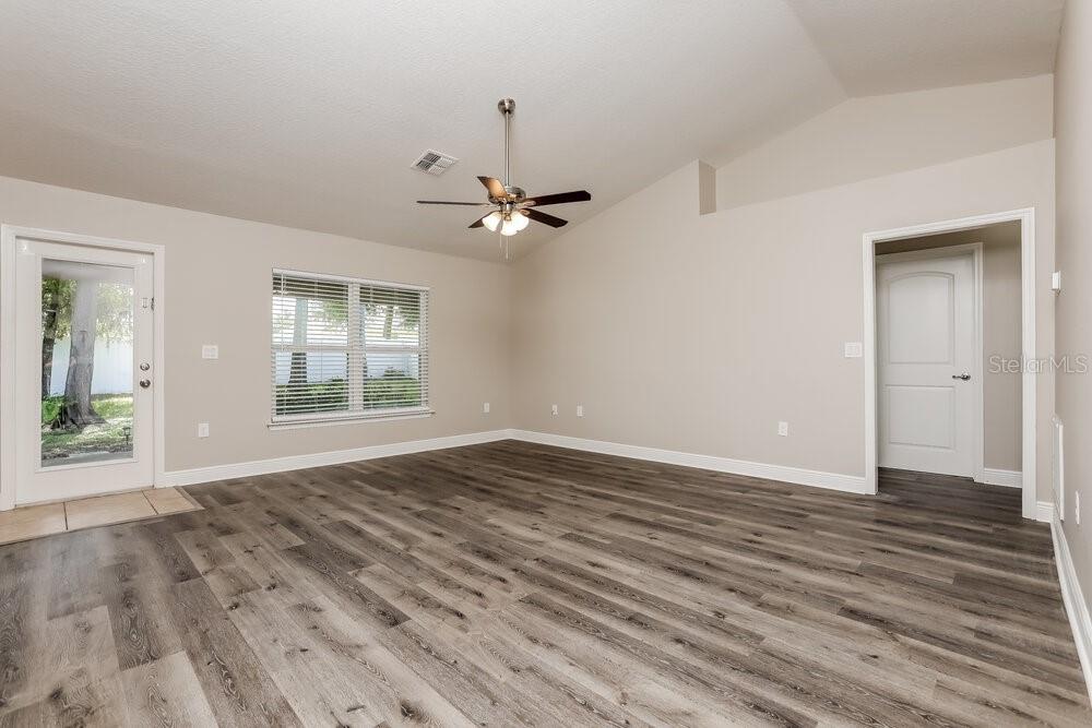 An empty living room features vaulted ceilings, wood-look flooring, a ceiling fan, and a window — 2214 ANGEL FISH LOOP, LEESBURG, FL