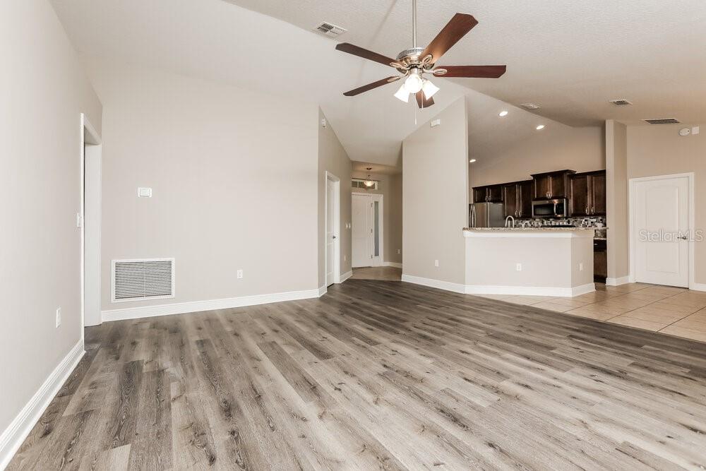 A living room with wood-look flooring, a ceiling fan, and an open kitchen area — 2214 ANGEL FISH LOOP, LEESBURG, FL