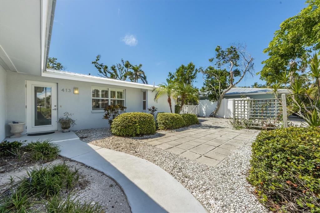 A light-colored house exterior features a concrete walkway, a stone patio, and manicured landscaping — 413 POINSETTIA ROAD, ANNA MARIA, FL