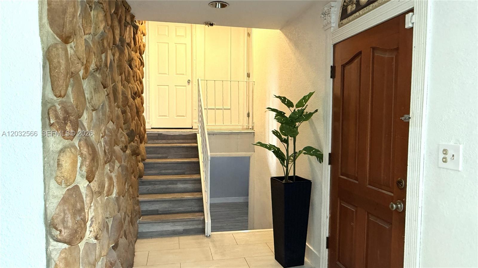 An entryway features a stone wall, a wooden door, and stairs leading to a landing — 1245 NE 203rd St, Miami FL 33179, MIAMI, FL