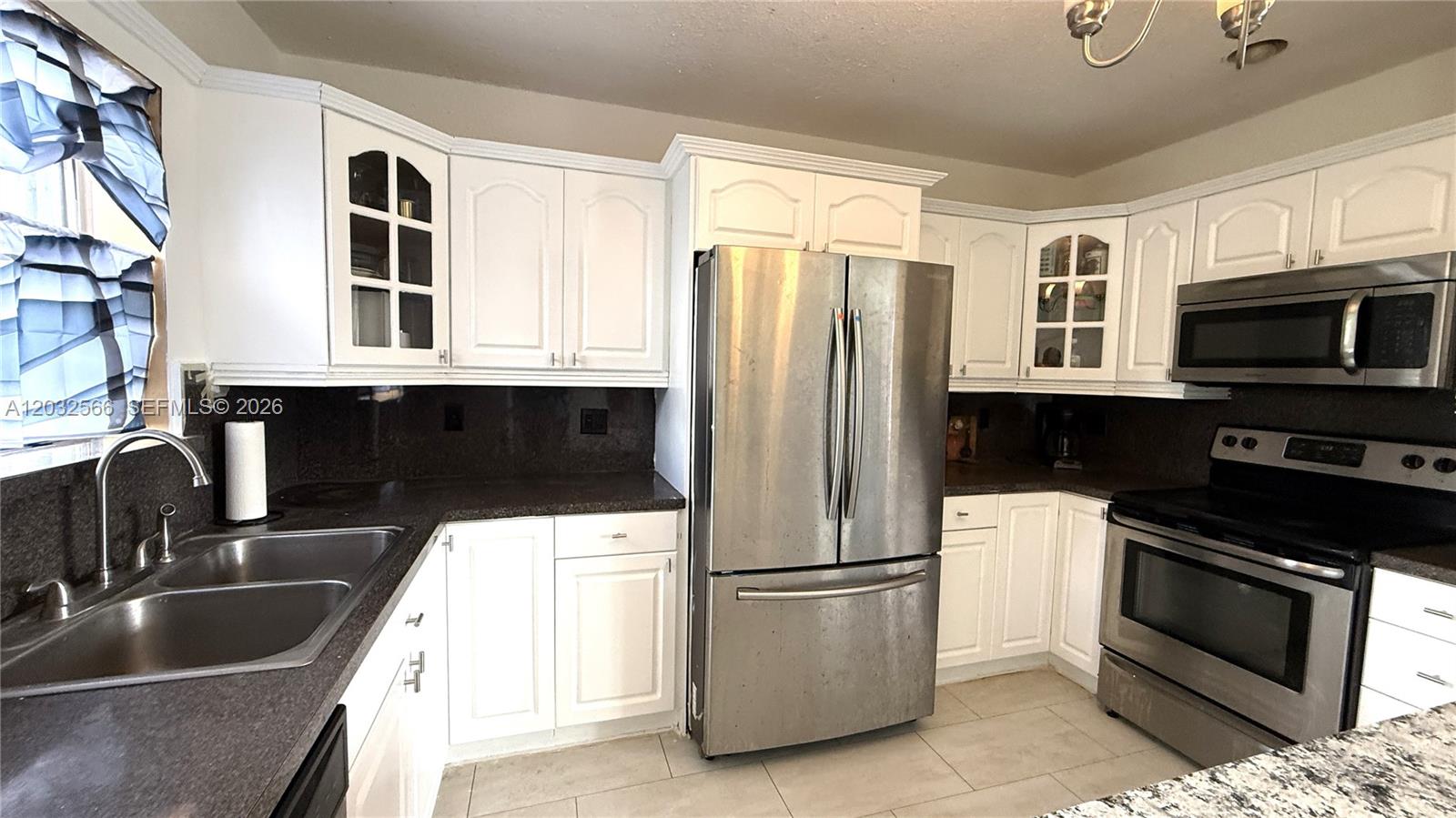 A kitchen features white cabinets, stainless steel appliances, and dark granite countertops — 1245 NE 203rd St, Miami FL 33179, MIAMI, FL