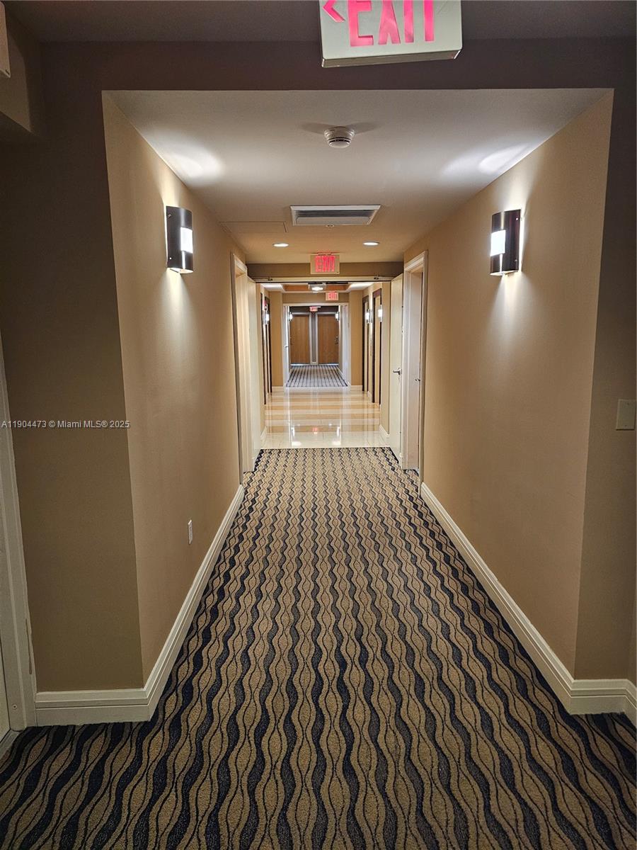 A long hotel hallway features patterned carpet, beige walls, wall sconces, and multiple exit signs — 244 Biscayne Blvd # 908, Miami FL 33132, MIAMI, FL