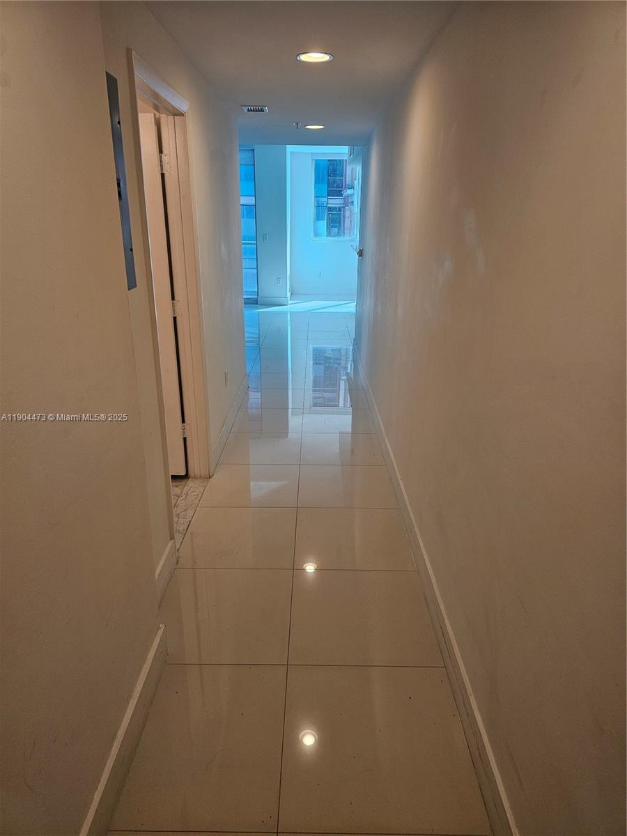 A narrow hallway with light-colored tile flooring leads toward a bright room with windows — 244 Biscayne Blvd # 908, Miami FL 33132, MIAMI, FL