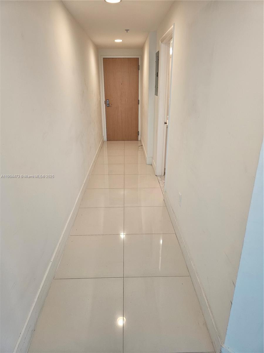 A narrow hallway features light-colored floor tiles and a wooden door at the end — 244 Biscayne Blvd # 908, Miami FL 33132, MIAMI, FL