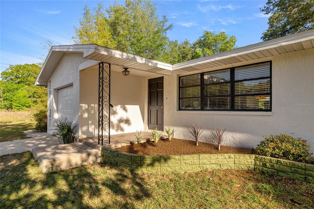 A single-story house exterior features a white stucco facade, a covered porch, and a garage — 20131 SW 83RD STREET, DUNNELLON, FL