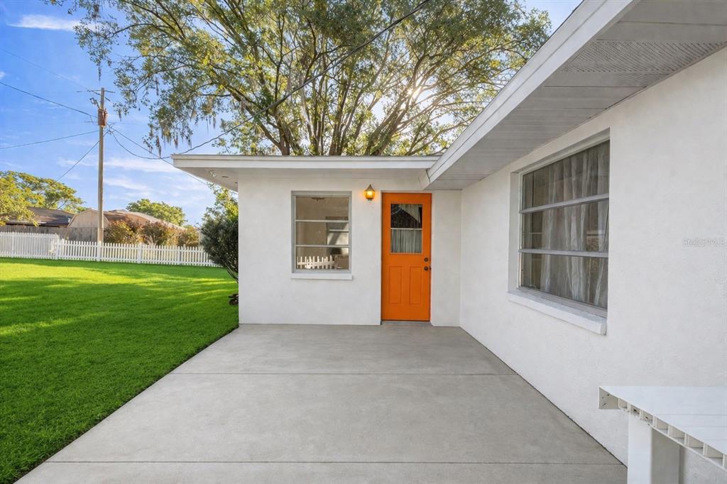 A concrete patio sits outside a white house with an orange door and large windows — 20131 SW 83RD STREET, DUNNELLON, FL