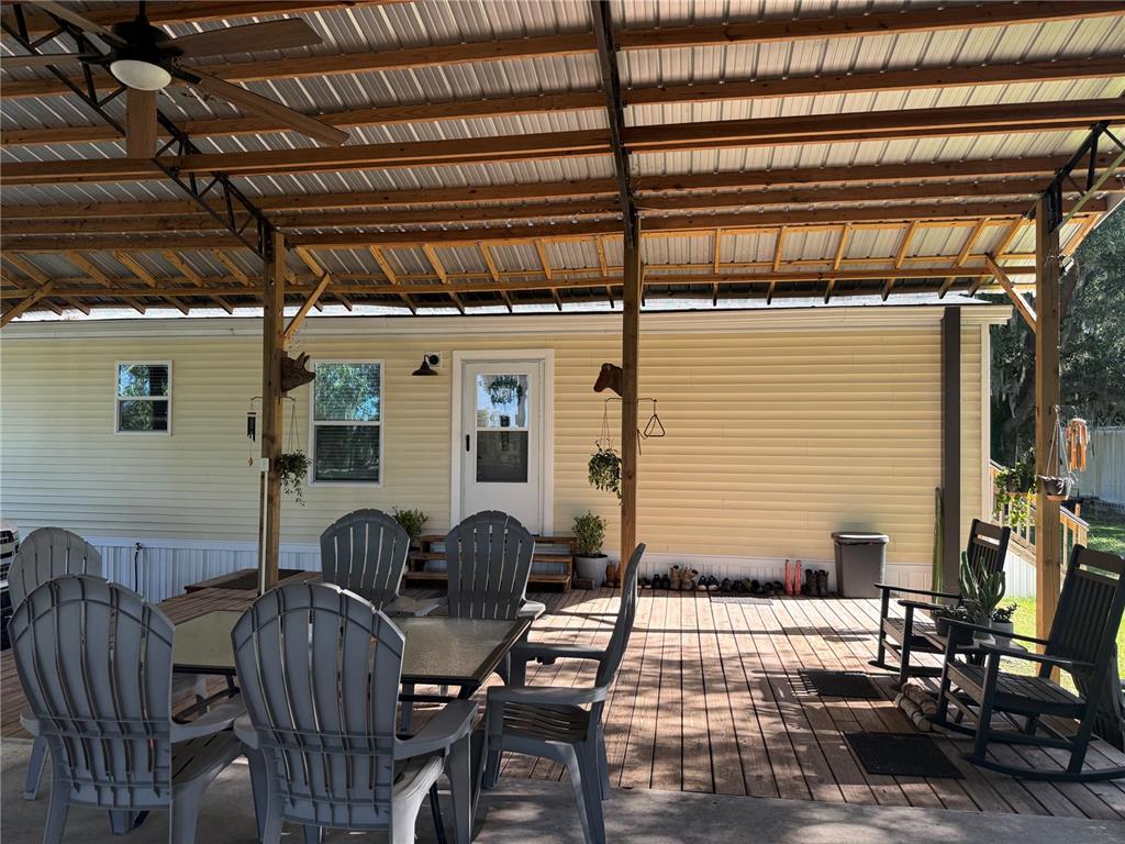 A covered wooden deck features a dining set, rocking chairs, and a yellow-sided home exterior — 4920 W KNIGHTS GRIFFIN ROAD, PLANT CITY, FL