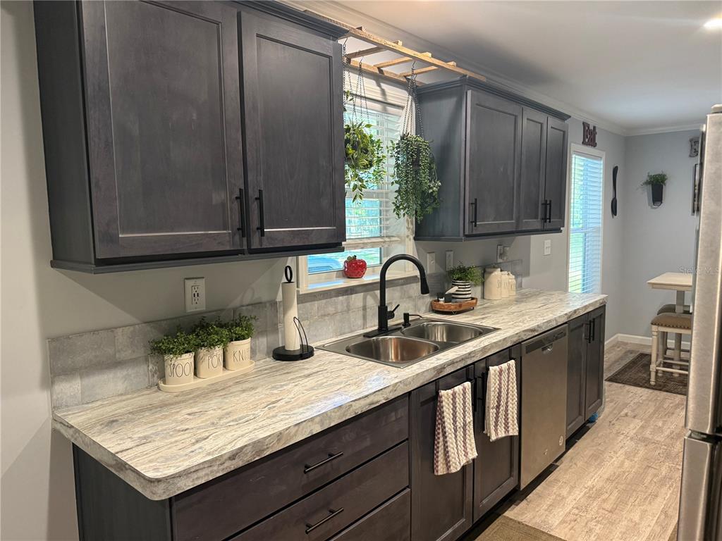 A kitchen features dark wood cabinets, a marble-patterned countertop, and a stainless steel dishwasher — 4920 W KNIGHTS GRIFFIN ROAD, PLANT CITY, FL