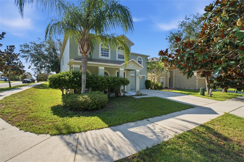 A two-story house with a palm tree, green lawn, and concrete driveway under a blue sky — 516 CADIZ DRIVE, GROVELAND, FL