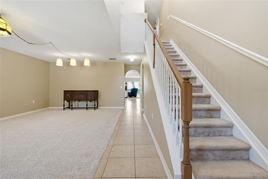 A carpeted living area with a wooden sideboard sits beside a staircase with carpeted steps — 516 CADIZ DRIVE, GROVELAND, FL