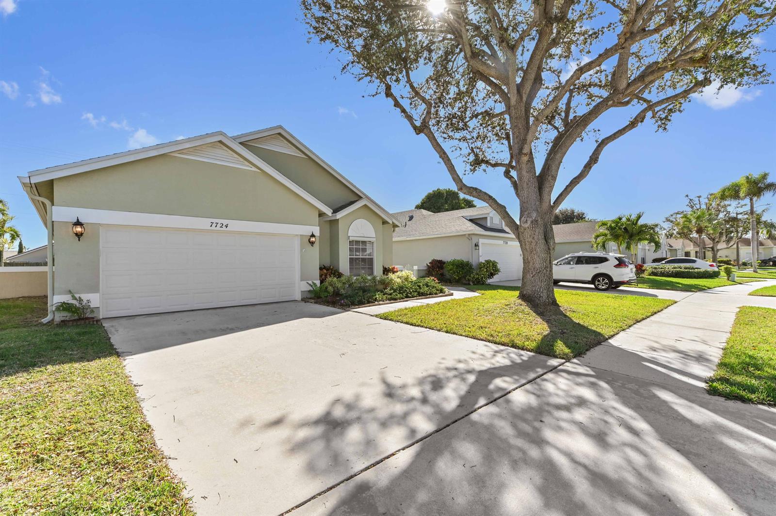 A light green single-story house with a two-car garage and a large front tree — 7724 Mansfield Hollow Road, Delray Beach FL 33446, DELRAY BEACH, FL
