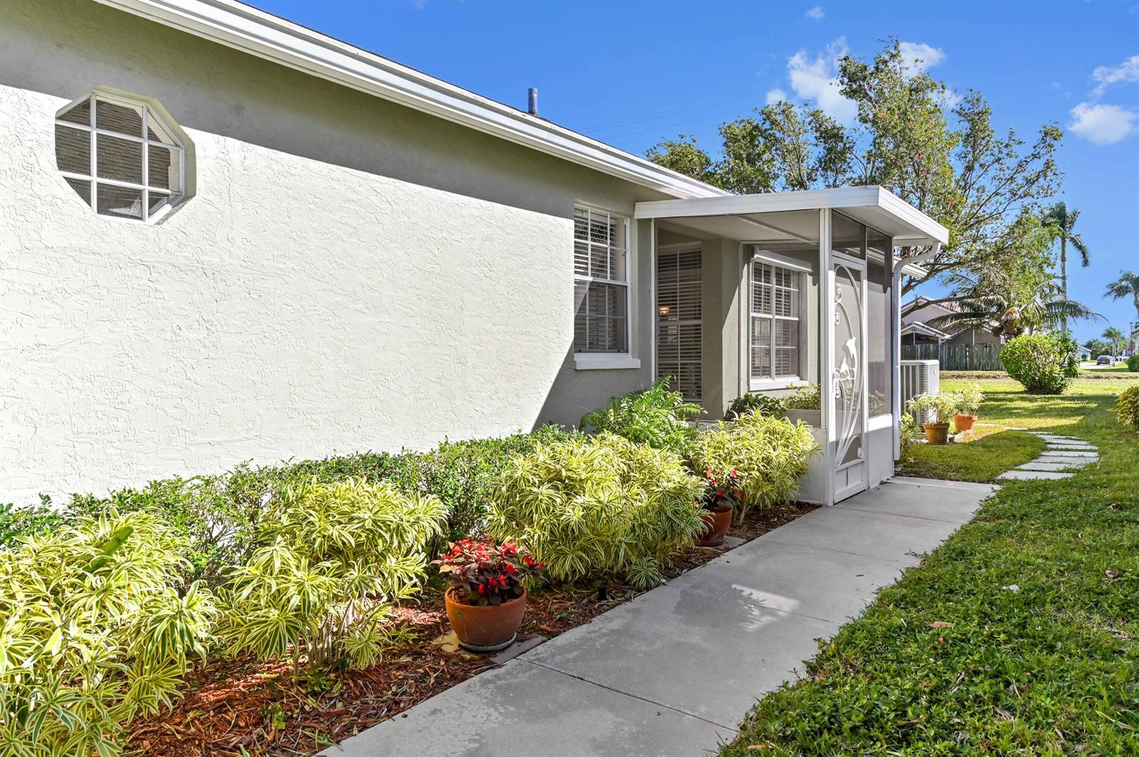 A side view of a house exterior with a screened porch and landscaped garden beds — 7724 Mansfield Hollow Road, Delray Beach FL 33446, DELRAY BEACH, FL
