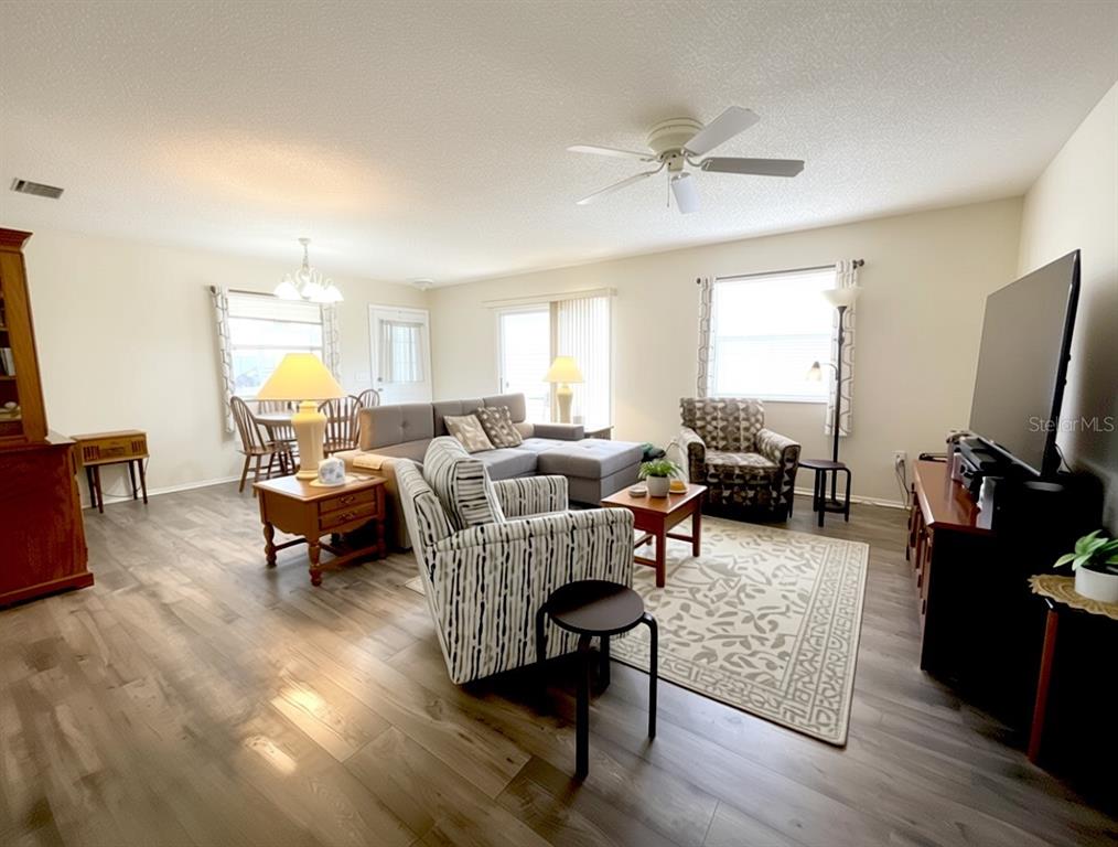 A living room features wood-look flooring, a ceiling fan, a television console, and two armchairs — 16938 SE 94TH SUNNYBROOK CIRCLE, THE VILLAGES, FL
