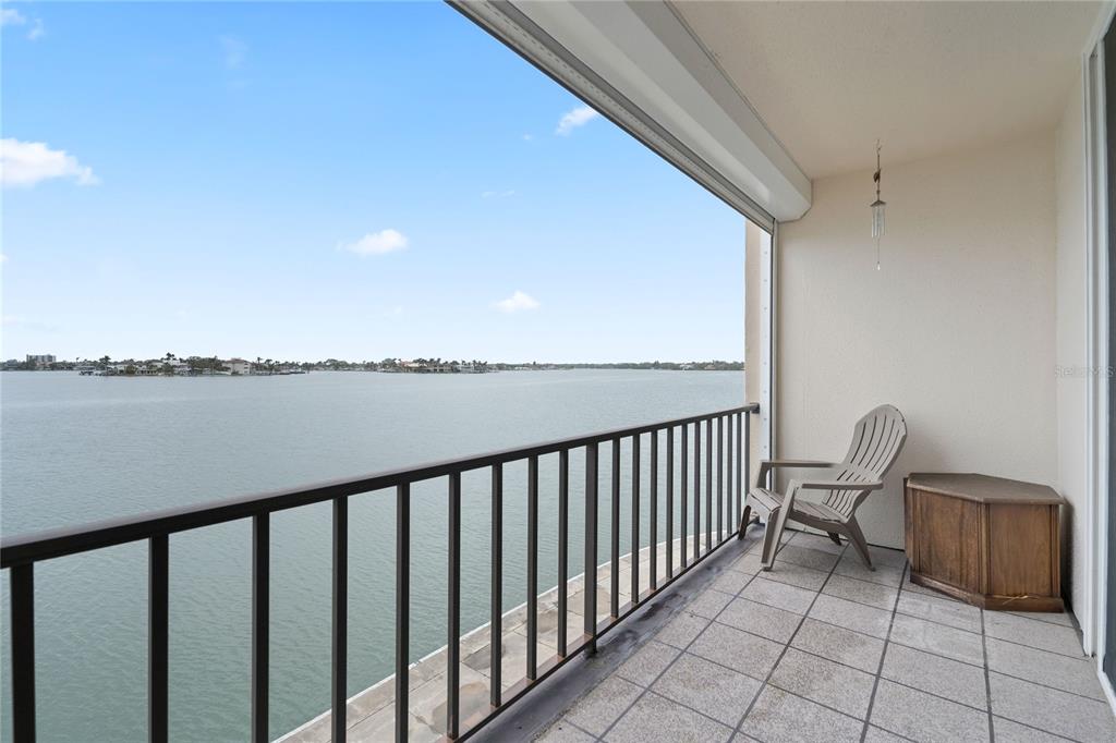 A balcony with a tiled floor, metal railing, and a chair overlooks a large body of water — 7910 SUN ISLAND DRIVE S UNIT 302, SOUTH PASADENA, FL