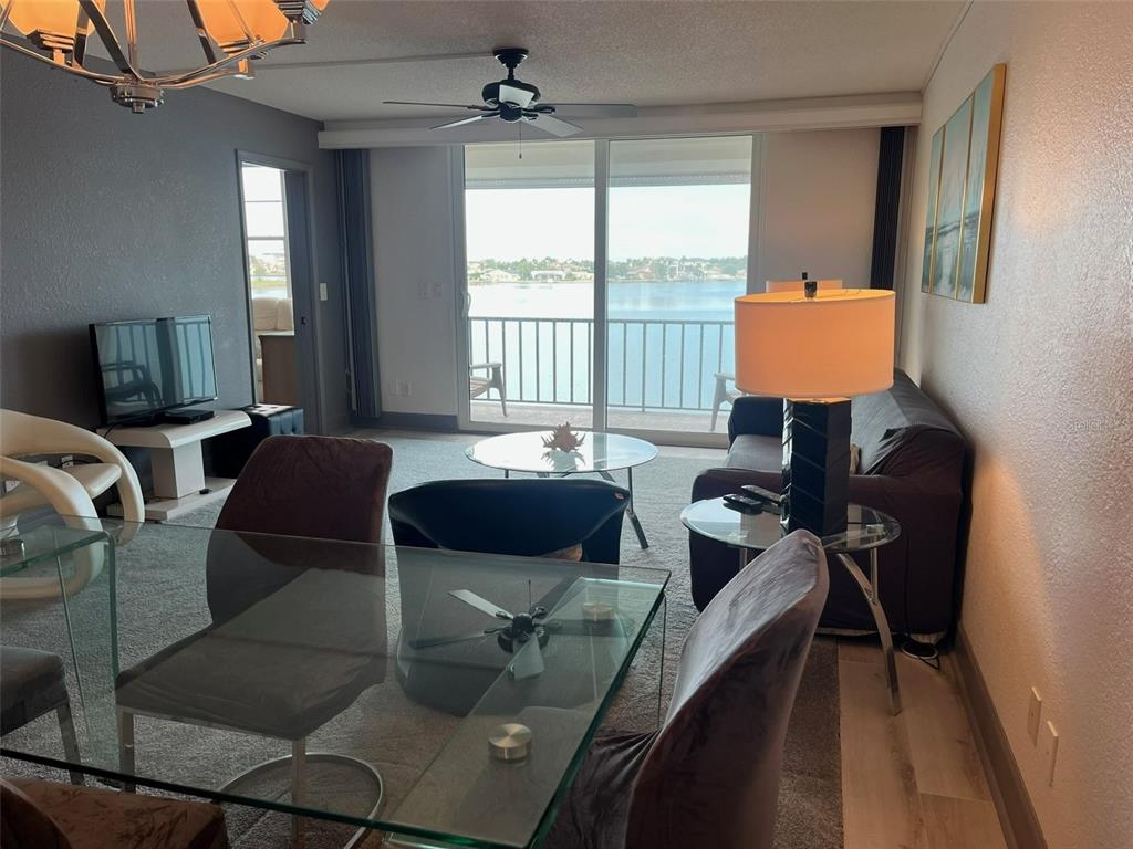 A living and dining area features a glass table, dark furniture, and a waterfront balcony view — 7910 SUN ISLAND DRIVE S UNIT 302, SOUTH PASADENA, FL