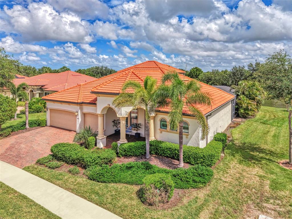An exterior view of a single-story house with a red tile roof and palm trees — 10908 BULLRUSH DRIVE, VENICE, FL