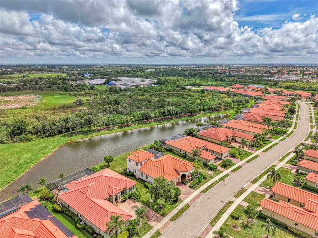 An aerial view shows a suburban neighborhood with red-tiled roofs, a pond, and green space — 10908 BULLRUSH DRIVE, VENICE, FL