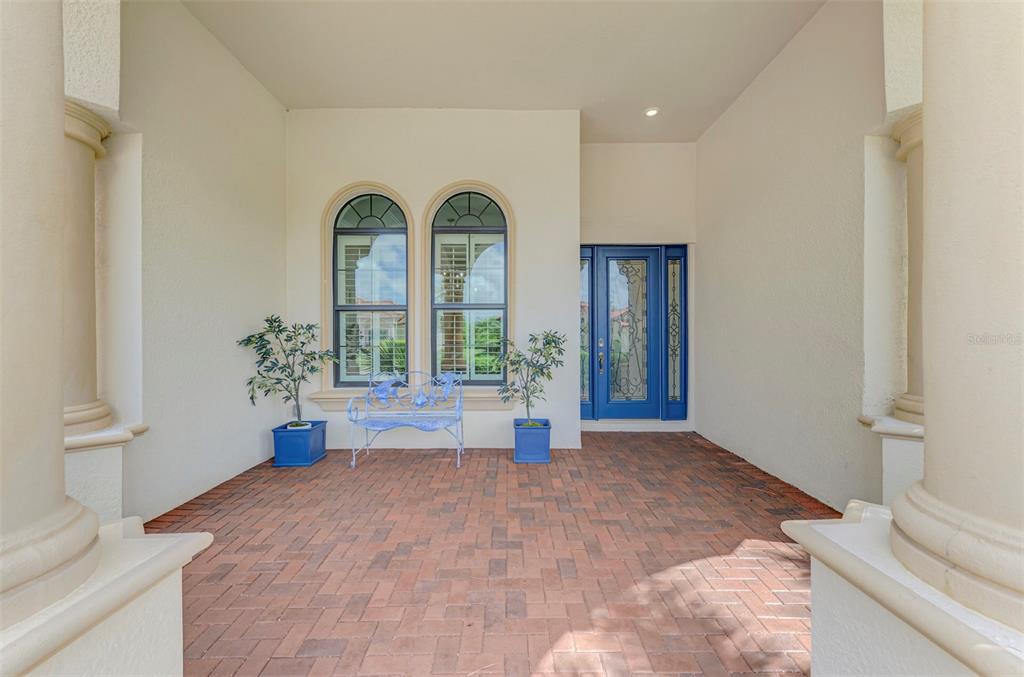 A covered brick porch features two arched windows, a blue bench, and a blue door — 10908 BULLRUSH DRIVE, VENICE, FL