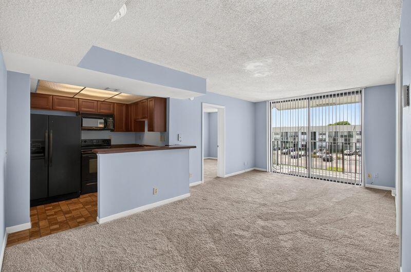A kitchen with dark cabinets and appliances opens into a carpeted living area with balcony access — 724 Executive Center Drive # 31, West Palm Beach FL 33401, WEST PALM BEACH, FL