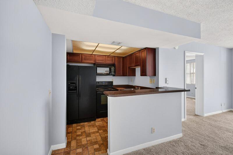 A kitchen with dark wood cabinets, black appliances, and a breakfast bar overlooks a carpeted room — 724 Executive Center Drive # 31, West Palm Beach FL 33401, WEST PALM BEACH, FL