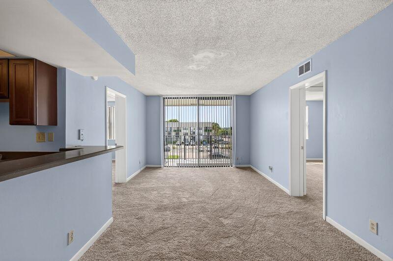 An empty living room with light blue walls, beige carpeting, and a sliding glass balcony door — 724 Executive Center Drive # 31, West Palm Beach FL 33401, WEST PALM BEACH, FL