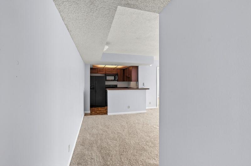 A view from a hallway looking into a kitchen with a breakfast bar and carpet — 724 Executive Center Drive # 31, West Palm Beach FL 33401, WEST PALM BEACH, FL