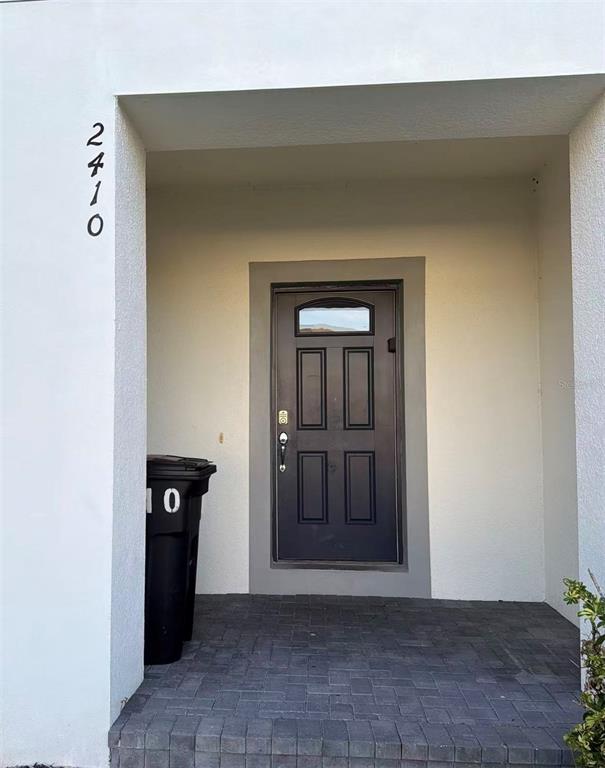 A dark front door is set within a recessed entryway with gray paver flooring — 2410 TANGIER DRIVE, KISSIMMEE, FL