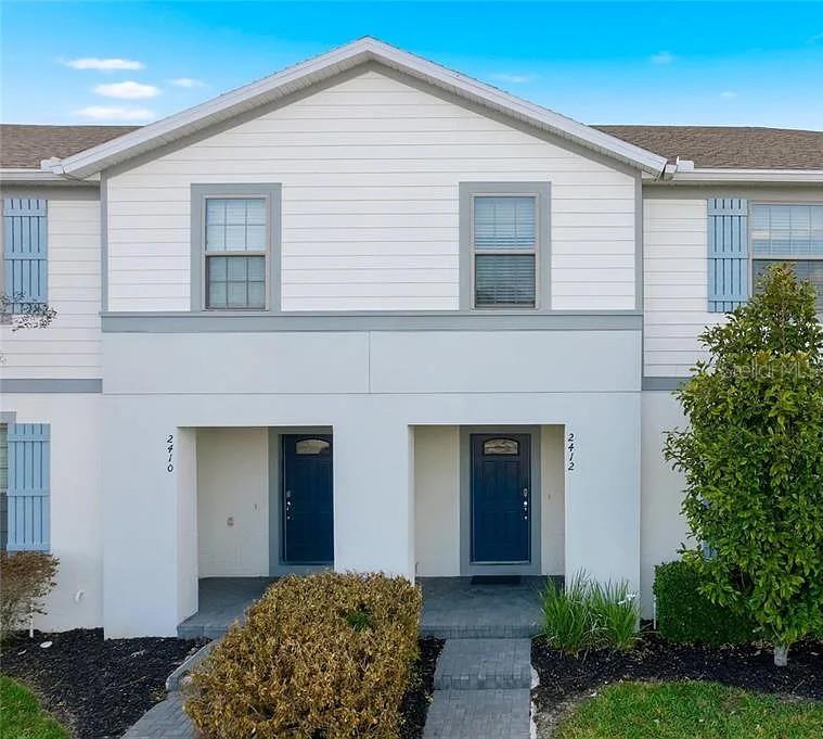 The exterior of a two-story townhouse features white siding, blue doors, and gray shutters — 2410 TANGIER DRIVE, KISSIMMEE, FL