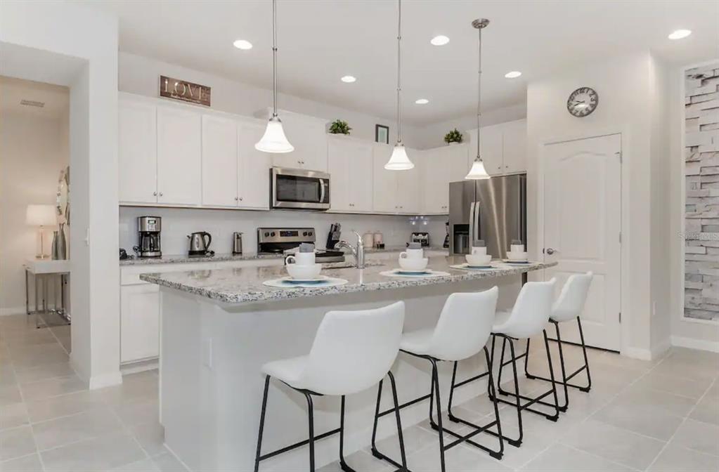 A modern kitchen features white cabinets, granite countertops, a central island, and four bar stools — 2410 TANGIER DRIVE, KISSIMMEE, FL