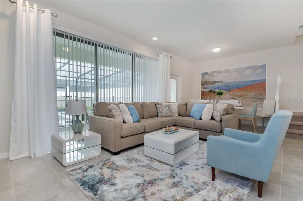 A living room features a beige sectional sofa, a blue armchair, and a patterned area rug — 2410 TANGIER DRIVE, KISSIMMEE, FL